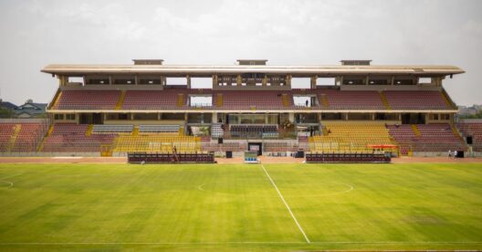 Estádio de futebol com bancadas vazias e relvado verde.