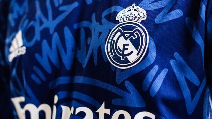Vista de close-up de uma camisa de futebol azul do Real Madrid apresentando o logo e elementos de design da equipe.