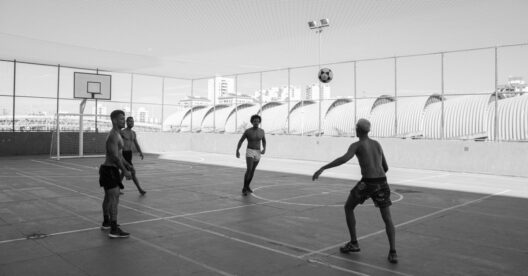 Jogadores de futebol a jogar numa quadra exterior com uma bola no ar.