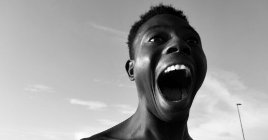 Homem negro a gritar com a boca aberta, com o céu ao fundo