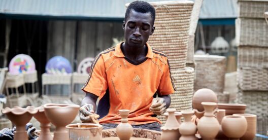 Artista africano criando vasos de barro feitos à mão em um mercado ao ar livre.