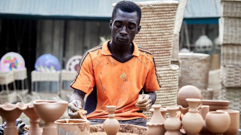 Artista africano criando vasos de barro feitos à mão em um mercado ao ar livre.