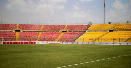 Uma vista ensolarada das arquibancadas vazias e da grama exuberante no Estádio Baba Yara em Kumasi, Gana.