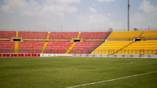 Uma vista ensolarada das arquibancadas vazias e da grama exuberante no Estádio Baba Yara em Kumasi, Gana.