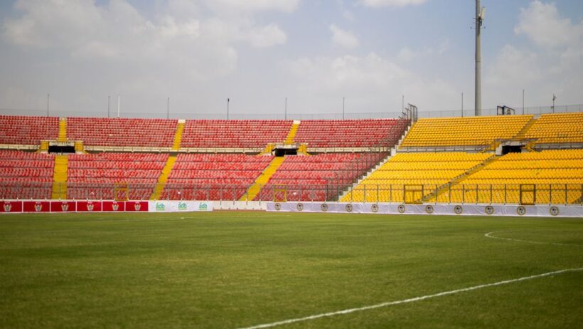 Uma vista ensolarada das arquibancadas vazias e da grama exuberante no Estádio Baba Yara em Kumasi, Gana.