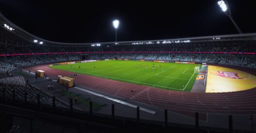 Estádio de futebol vazio, bem iluminado, com campo verde sob os holofotes durante a noite.