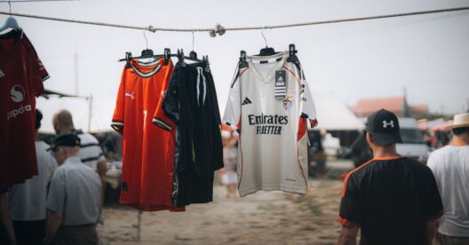 Camisolas de futebol do Milan e do Benfica penduradas numa corda, com pessoas ao fundo.