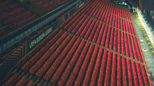 Fileiras de assentos vermelhos vazios em um estádio da Liga Europa da UEFA, fotografadas de cima.