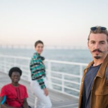 Grupo de pessoas diversas, incluindo uma em cadeira de rodas, em um cais ao pôr do sol.
