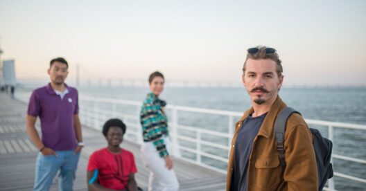 Grupo de pessoas diversas, incluindo uma em cadeira de rodas, em um cais ao pôr do sol.