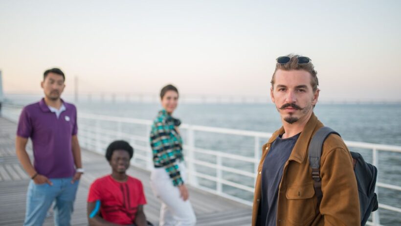 Grupo de pessoas diversas, incluindo uma em cadeira de rodas, em um cais ao pôr do sol.