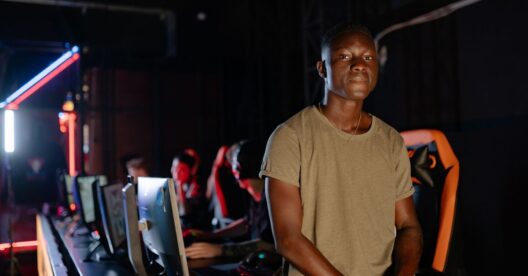 Jovem adulto num centro de jogos com computadores ao fundo.